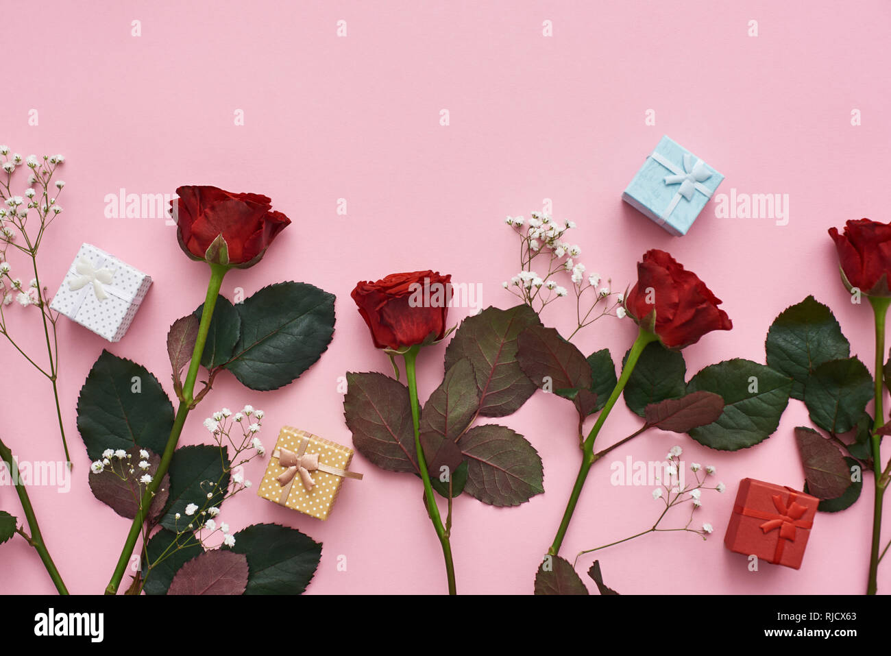 Die wahre Liebe. Zeigen Sie Ihre Gefühle mit roten Rosen, niedliche Geschenkboxen und zarten Wildblumen. Rosa Hintergrund Stockfoto