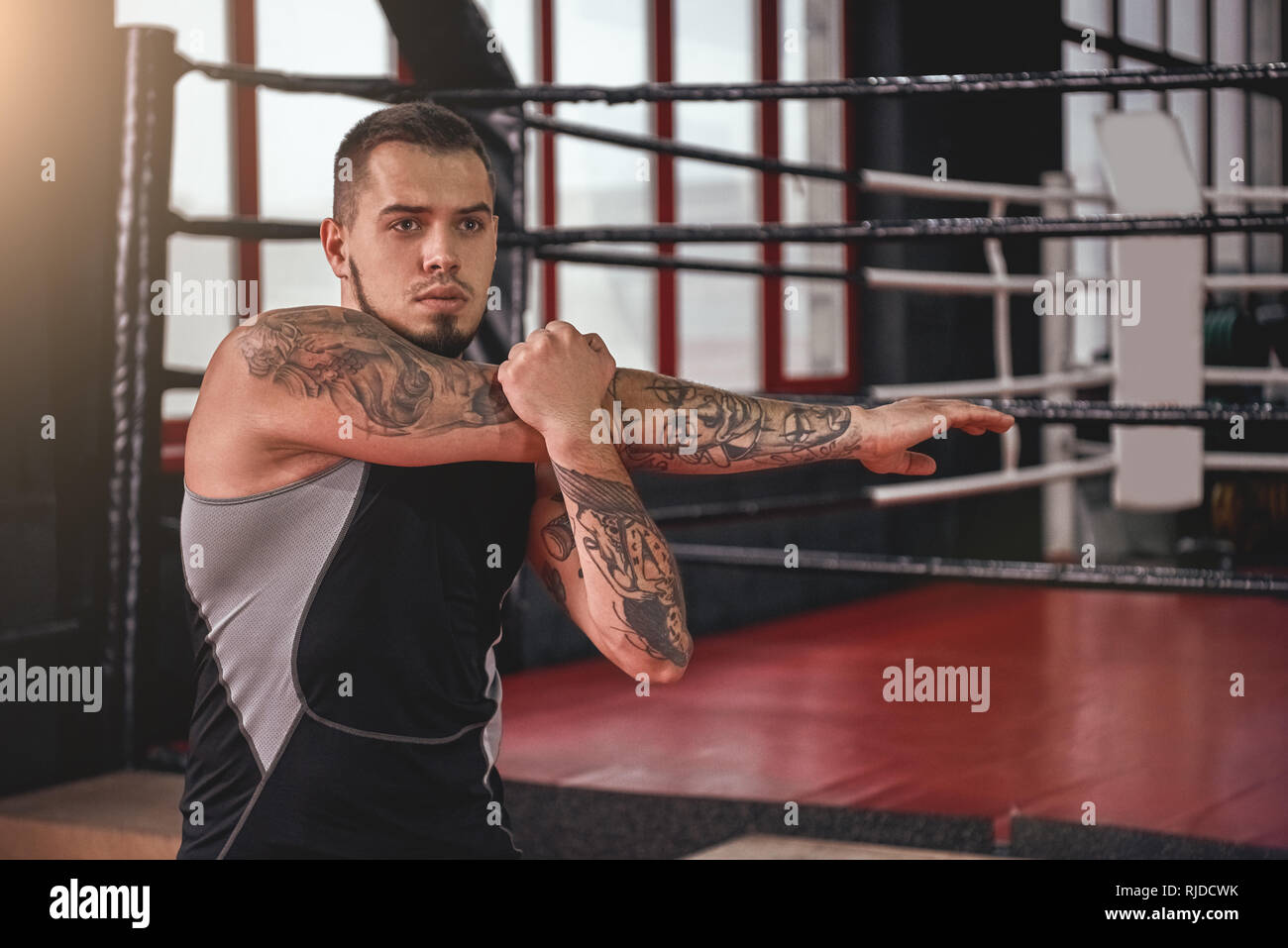 Schwerpunkt junge muskulöse Athleten in farbigen Sport Kleidung suchen, während seine Muskeln Aufwärmen vor dem Training in schwarz Boxing Gym Stockfoto