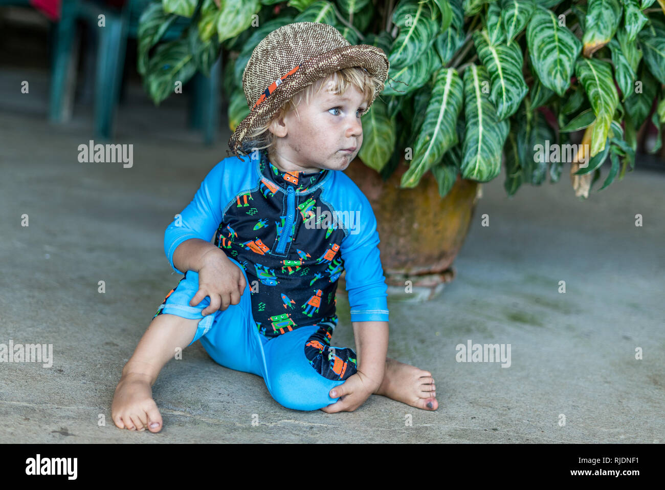 Ein schönes Porträt einer niedlichen Hut tragen baby boy vor einem wunderschönen tropischen Blume posieren. Der Junge trägt einen UV-Schutz. Stockfoto