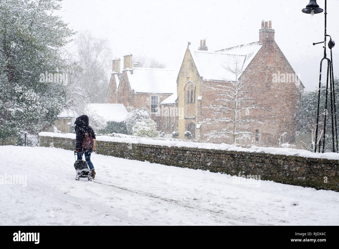 Dame ziehen Einkaufswagen auf schneebedeckten St. Andrew's Street in Wells, Somerset, Großbritannien Stockfoto