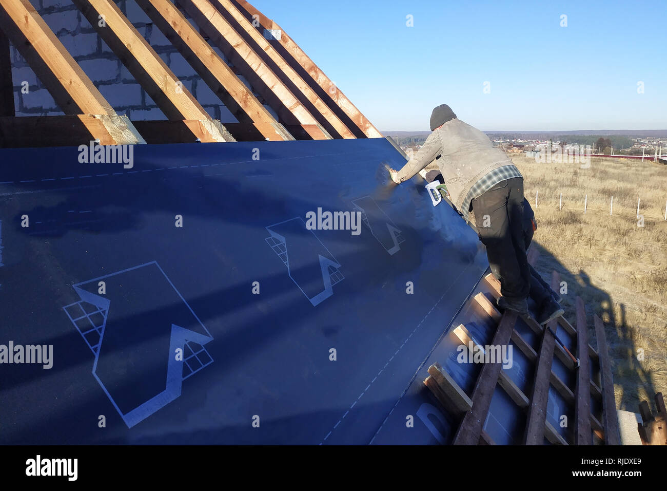 Arbeiter auf dem Dach des Hauses eine wasserfeste Folie unter dem Dach  anbringen und mit einem Hefter 2019 sichern Stockfotografie - Alamy