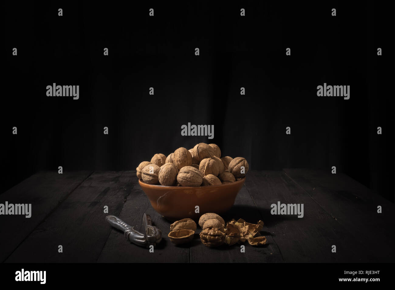 Walnüsse in eine Schüssel auf dunklem Hintergrund. Low-key-Bild der Muttern auf Schwarz rustikale Tische, Licht und Schatten Technik und festplattenobjekte Tempo Stockfoto