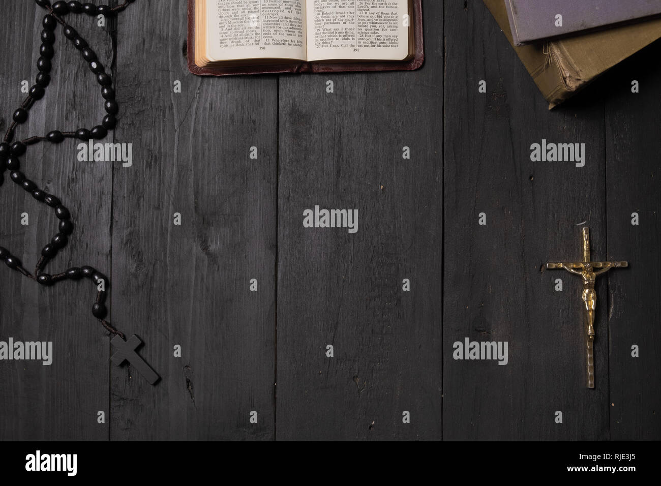 Buch der Bibel und Kruzifix auf dunklen Relation geöffnet, Ansicht von oben. Flach Bild des Neuen Testaments, Kreuz und Rosenkranz auf dem alten schwarzen Hintergrund Stockfoto