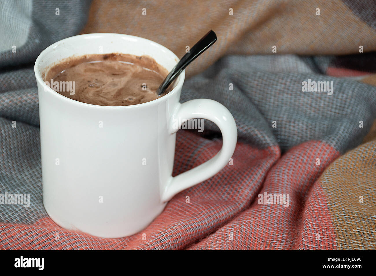 Nahaufnahme der heißen Kakao trinken in weiße Tasse mit schwarzem Löffel und weiche Decke Stockfoto