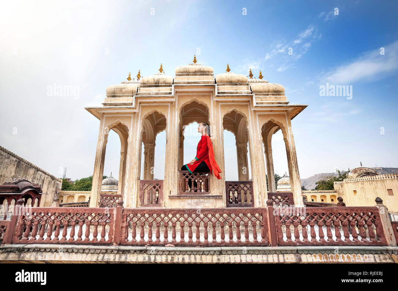 Die Frau im roten Kleid mit Schal auf der dekorativen Royal Balkon in Hawa Mahal, Rajasthan, Indien sitzen Stockfoto