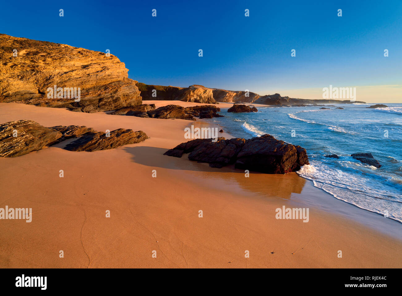 Einsamer Strand mit Sand und Felsen entlang einer ruhigen blauen Ozean mit weichen Wellen Stockfoto