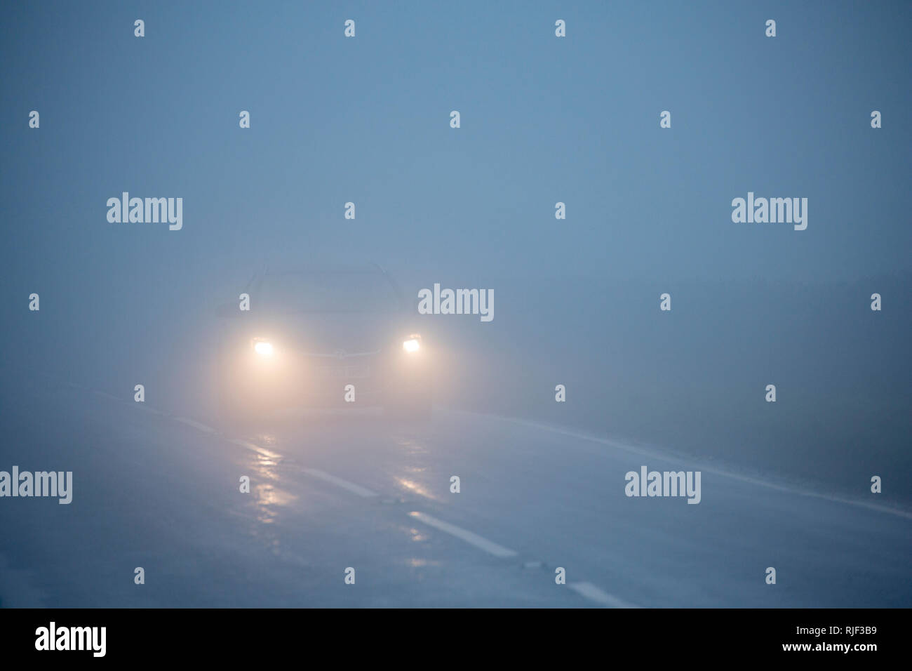 Ein Auto mit seinen Scheinwerfer auf langsamer Fahrt in dichtem Nebel am Nachmittag im Februar. North Dorset England UK GB Stockfoto