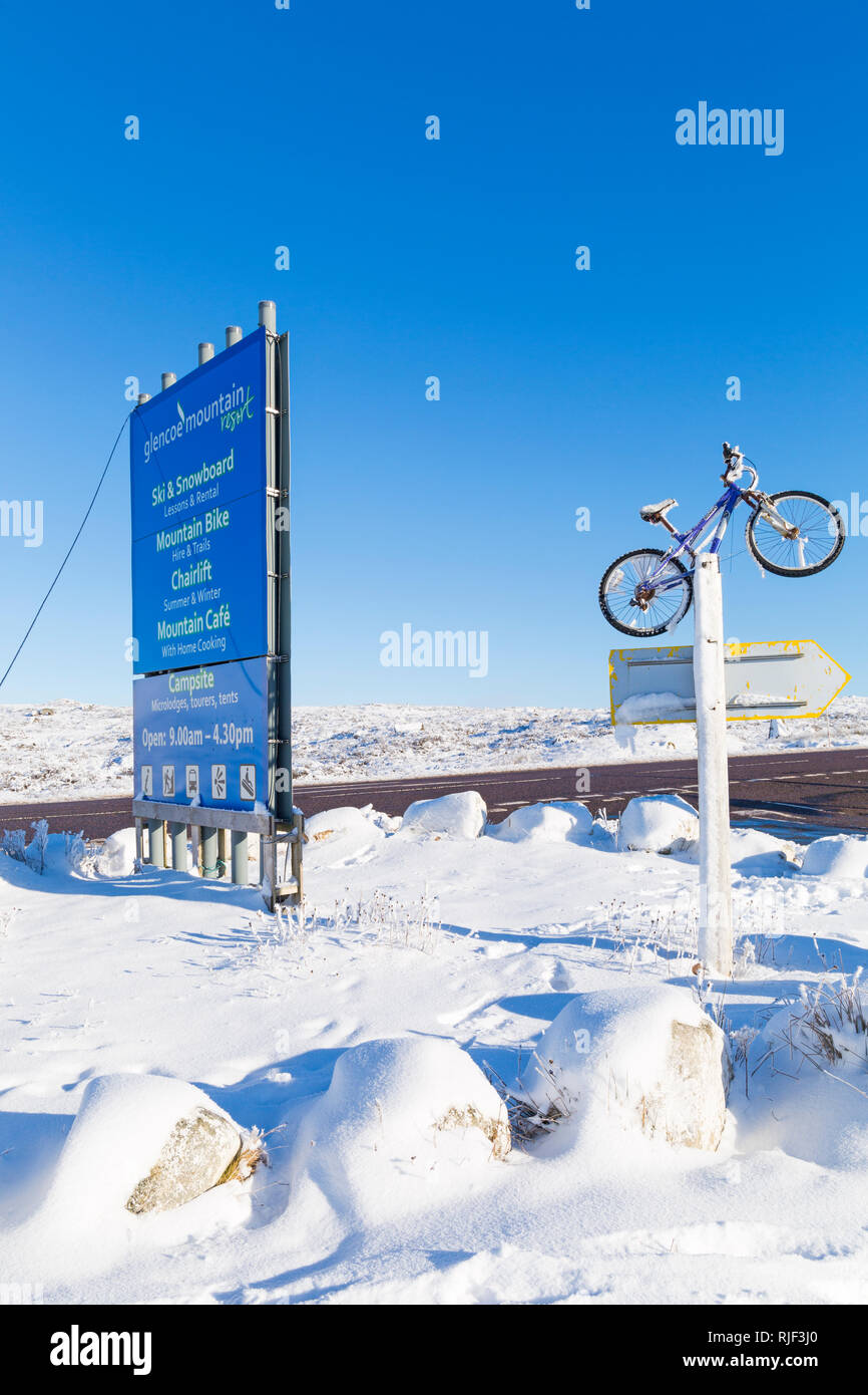 Zeichen und Mountainbike am Eingang an der A82 für das Drehen nach Glencoe Mountain Resort in Glencoe, Highlands, Schottland im Winter Stockfoto