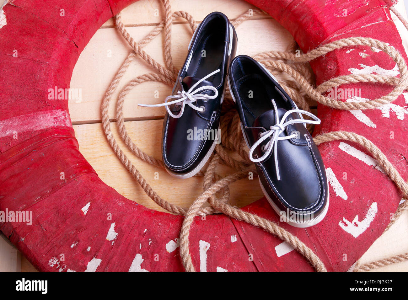 Blau Boot Schuhe auf hölzernen Hintergrund in der Nähe von Red Rettungsring und Seil. Ansicht von oben. Stockfoto