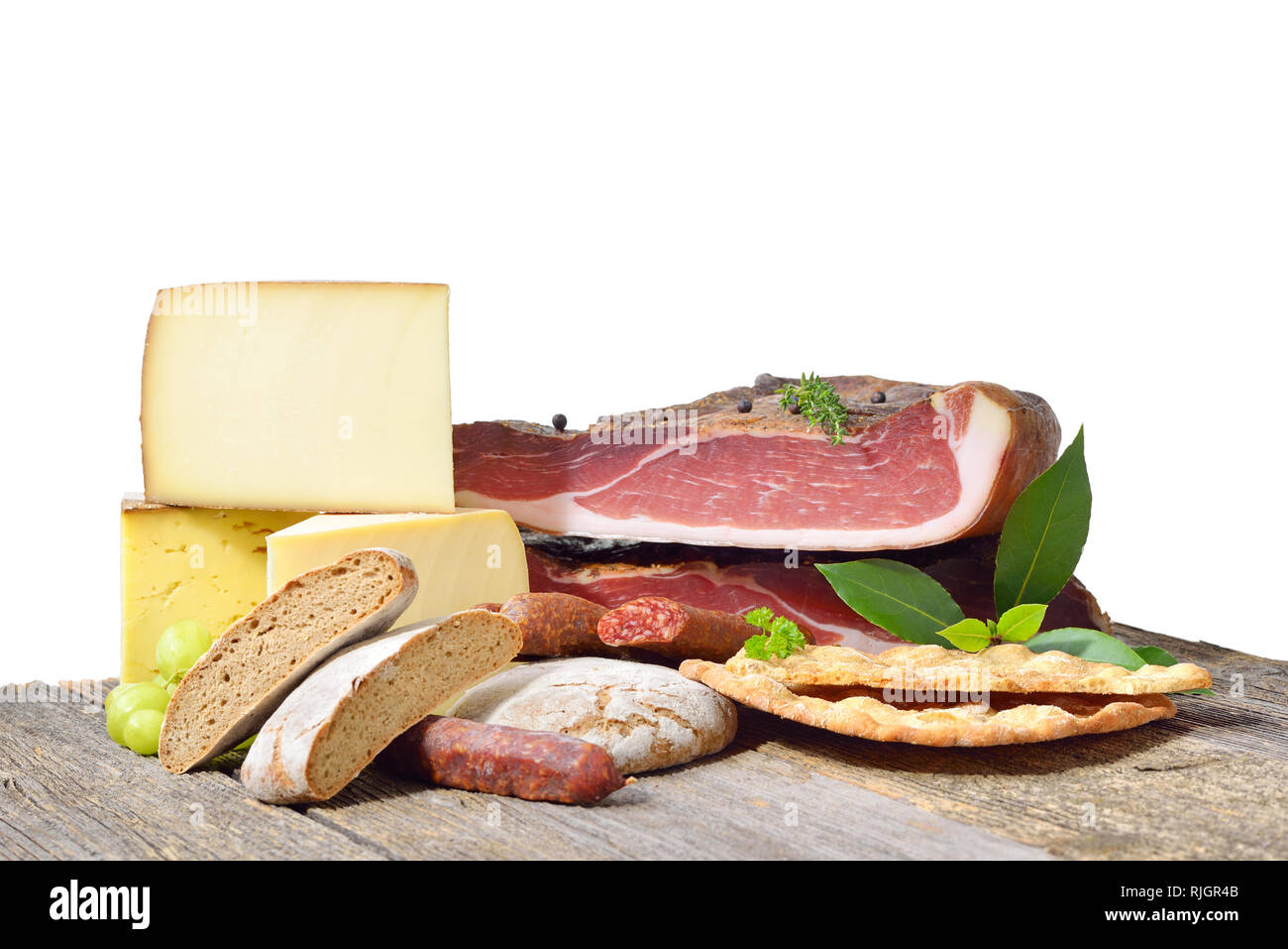 Südtiroler Spezialitäten wie Speck, wurst und Käse liegen auf einem rustikalen Tisch vor einem weißen Hintergrund Stockfoto