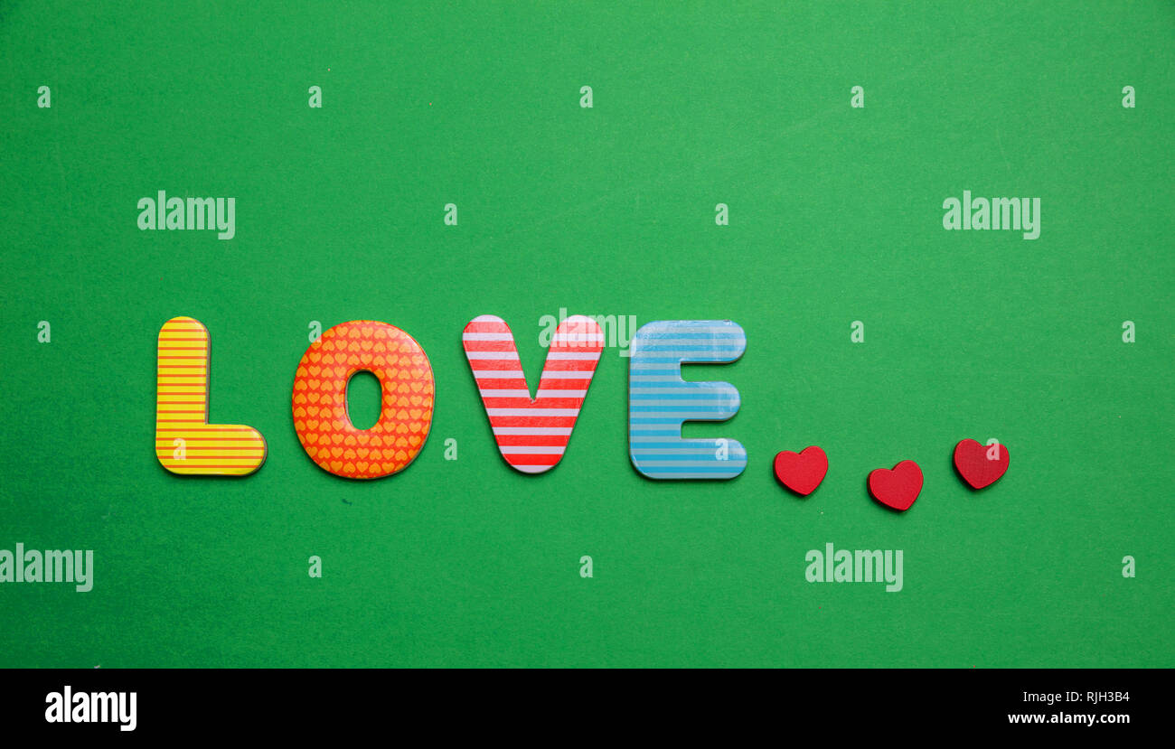 Liebe Text mit bunten Buchstaben und kleinen roten Herzen auf grüne Farbe Hintergrund Stockfoto