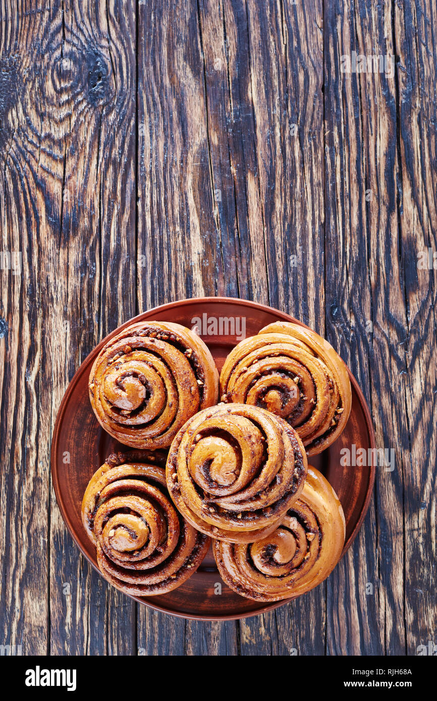 Frisch gebackenen Zimtschnecken Brötchen mit Erdnüssen auf einem Steingut Teller serviert. Kanelbulle schwedische Dessert, vertikale Ansicht von oben, Kopie Raum Stockfoto