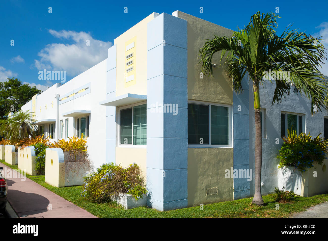 Palmen und tropischen Pflanzen schmücken die Fassade eines einfachen 1-stöckigen Art-Deco-Gebäude unter strahlend blauen Himmel in South Beach, Miami, Florida Stockfoto
