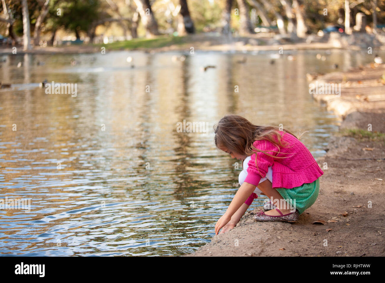 Junge Mädchen an einem Seeufer mit den Händen berühren das Wasser kniet. Stockfoto