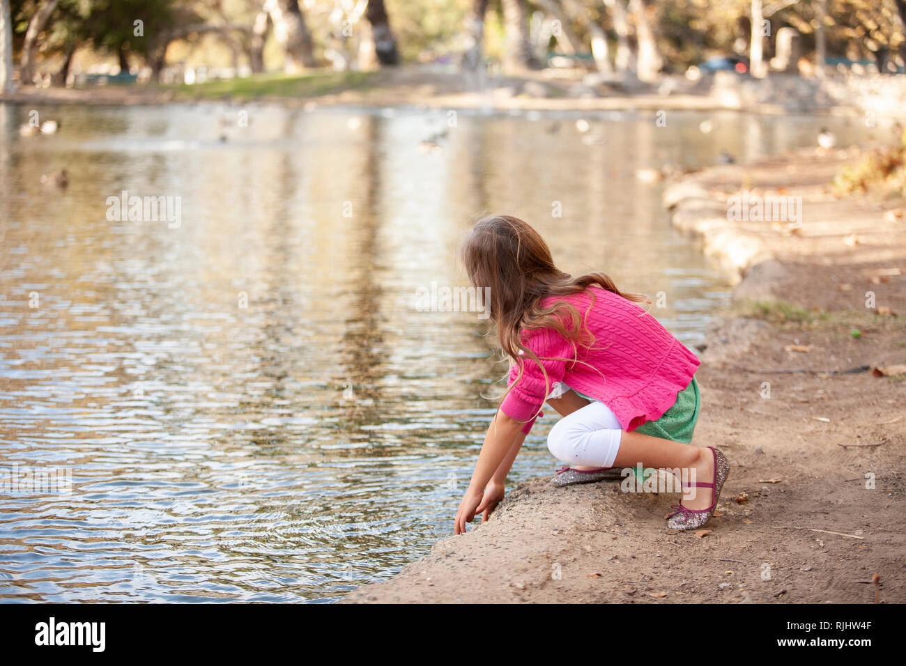Junge Mädchen an einem Seeufer mit den Händen berühren das Wasser kniet. Stockfoto