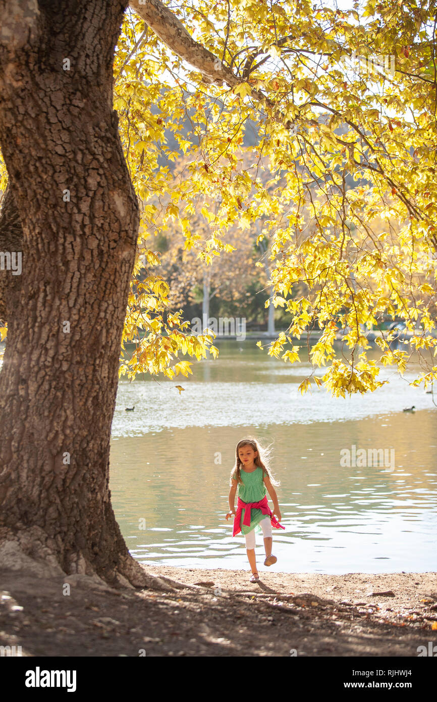 Junge Mädchen zu Fuß in Richtung Kamera mit einem See und Herbst Baum im Hintergrund Stockfoto