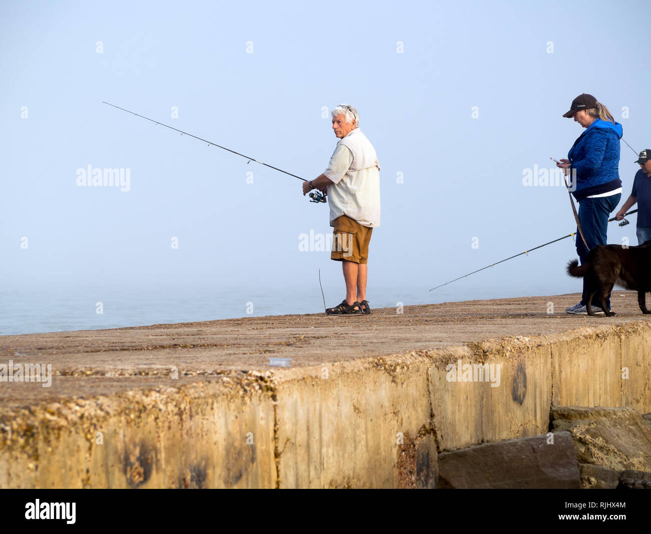 Eine silberhaarige Mann in Shirt, Shorts und Sandalen Fische aus dem Süden Anlegestelle an einem nebligen gekleidet, Februar Tag in Port Aransas, Texas USA. Stockfoto