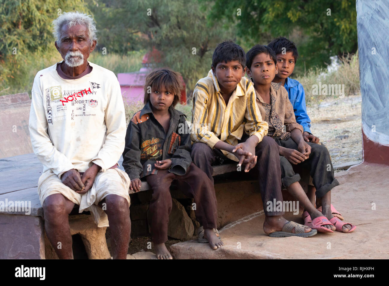 Bhil tribespeople. Ein älterer Mann sitzt mit vier Jungen in ihrem Dorf in der Nähe von Bhainsrorgargh, Rajasthan, Indien. Stockfoto