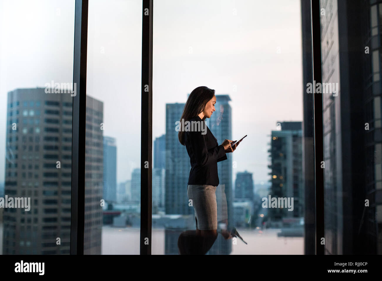 Geschäftsfrau, die spät mit Sicht auf die City Skyline im Hintergrund Stockfoto