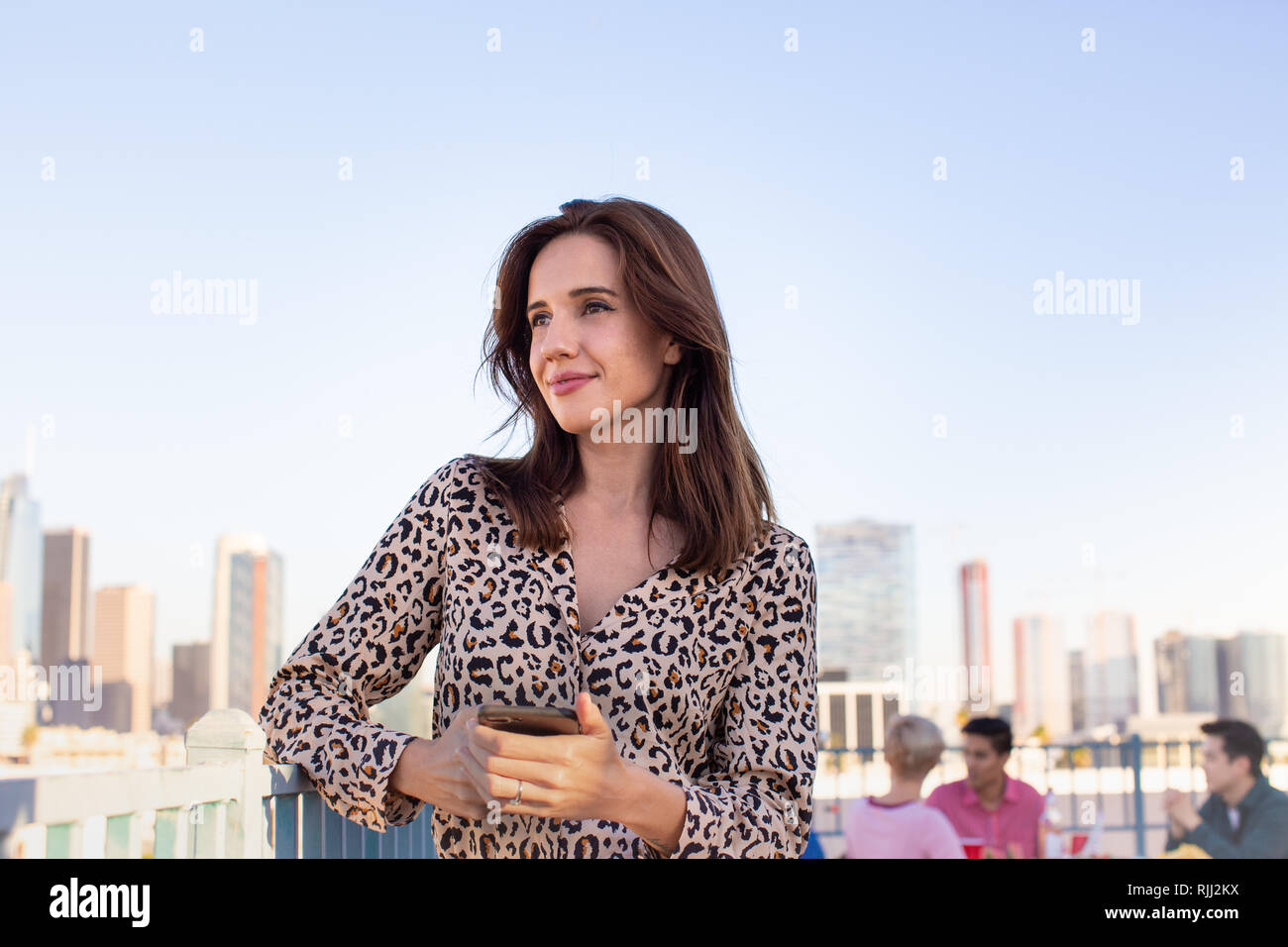 Junge erwachsene Frau mit Blick über die Stadt auf eine Dachterrasse mit Partei Stockfoto