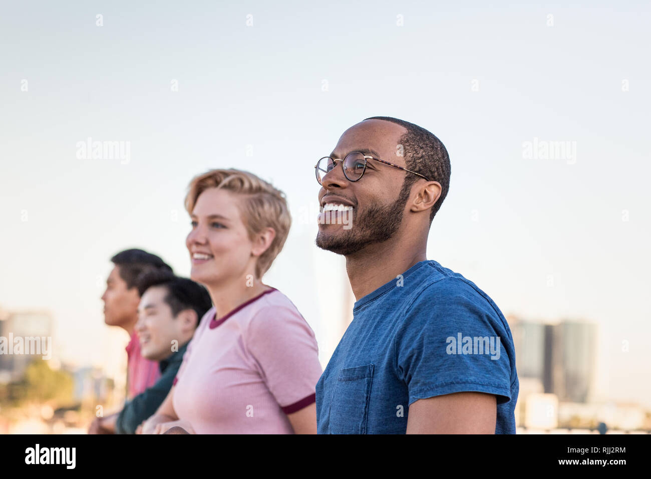 Eine Gruppe von Freunden mit Blick auf die Skyline der Stadt, die auf einem Dach Stockfoto