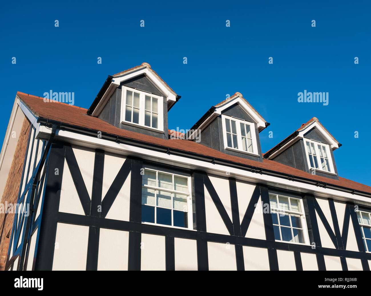 Drei Dachgauben in das Dach einer Tudor Stil schwarze und weiße Englisch Wohnhaus vor blauem Himmel. Das Haus verfügt über Schiebefenster und weichen Matte Stockfoto