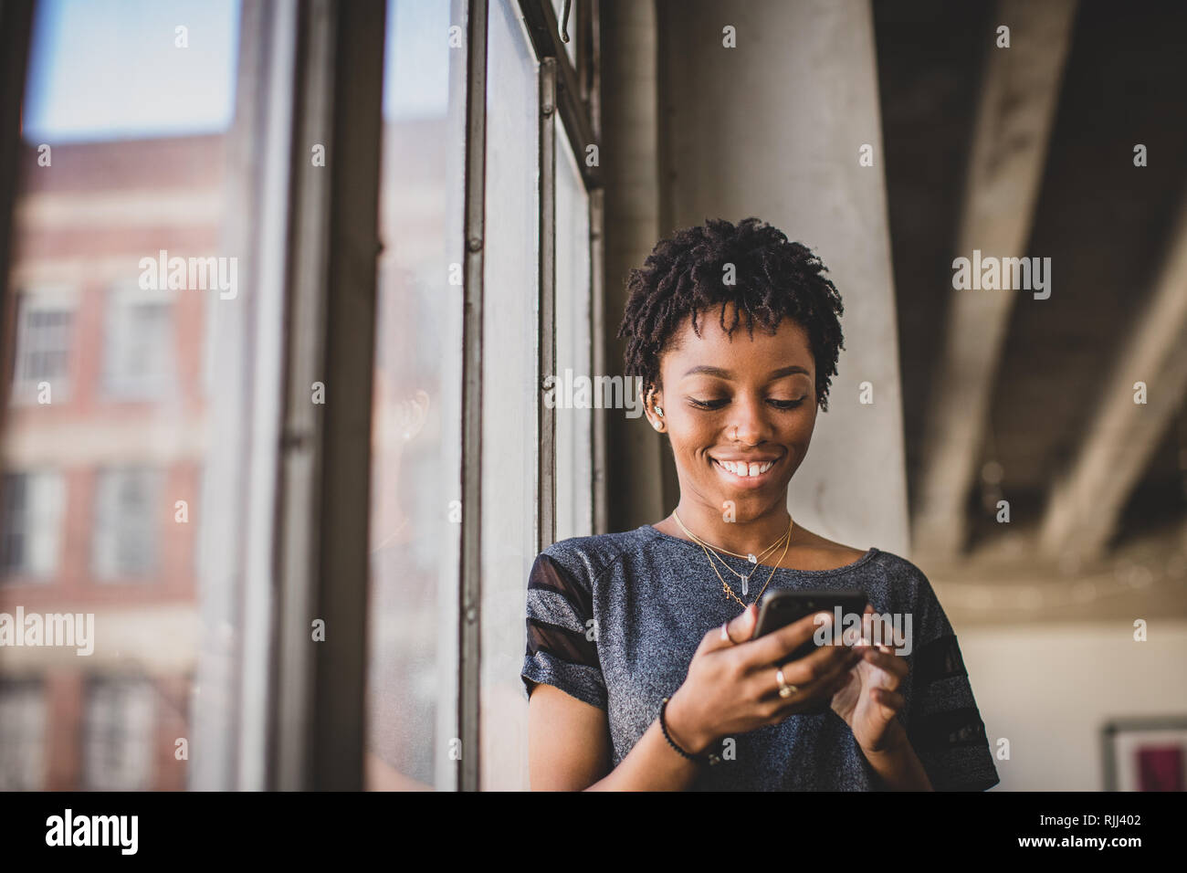 Junge afrikanische amerikanische weibliche in loft apartment Blick auf Smartphone Stockfoto