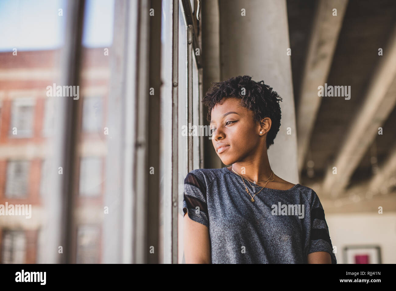 Junge afrikanische amerikanische weibliche Blick aus Fenster in loft apartment Denken Stockfoto