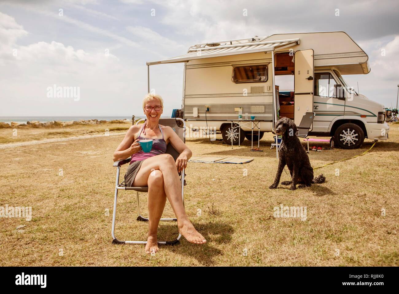 Frau sitzt mit einem Hund, König Pudel, vor ihr Wohnmobil und Kaffee  trinken während der Ferien am Meer, Denneville, Normandie Stockfotografie -  Alamy