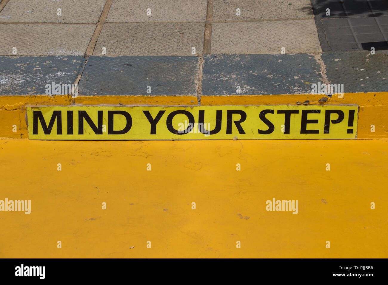 Kümmern sie sich um Ihre schritt Warnschild auf einem Gehsteig in hellem Gelb Bild mit Kopie Raum im Querformat. Stockfoto