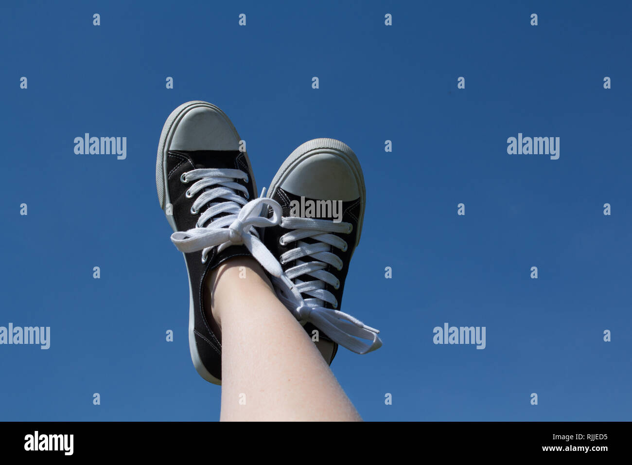 Ein Foto von einer weiblichen Füße mit Turnschuhen in die Luft gehoben mit einem strahlend blauen Himmel über. Das Gefühl ist sorglos. Stockfoto
