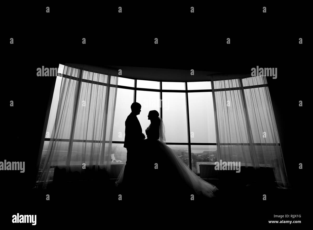 Silhouetten der Hochzeit paar Umarmen im Hotel Zimmer in der Nähe der Fenster. Schwarz und Weiß. Stockfoto