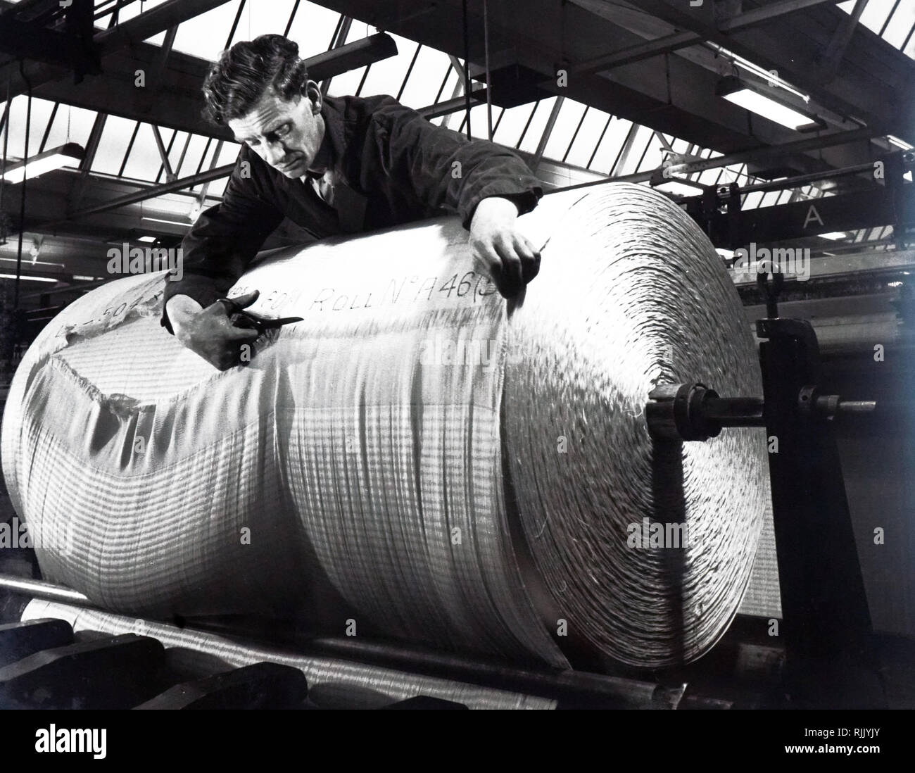 Ein Foto von einem Mann schneidet eine ausgefüllte Rolle von Reifencord aus Tenasco (Courtaulds hochfesten Viskosegarnen Garne). Vom 20. Jahrhundert Stockfoto