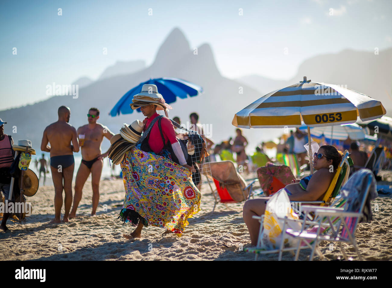 RIO DE JANEIRO - Februar, 2018: Ein Strand Anbieter verkaufen hell gemusterten canga Sarongs und Hüte Spaziergänge Seine waren am Strand von Ipanema. Stockfoto