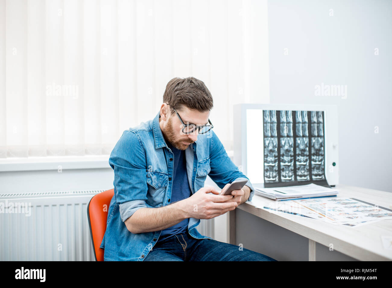 Mann mit Smartphone nach unten gebeugt sitzen in die Skoliose im Büro des Therapeuten in der Klinik Stockfoto