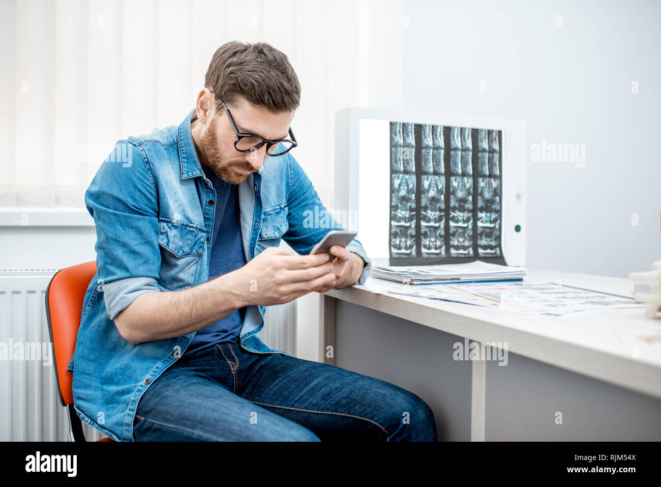 Mann mit Smartphone nach unten gebeugt sitzen in die Skoliose im Büro des Therapeuten in der Klinik Stockfoto