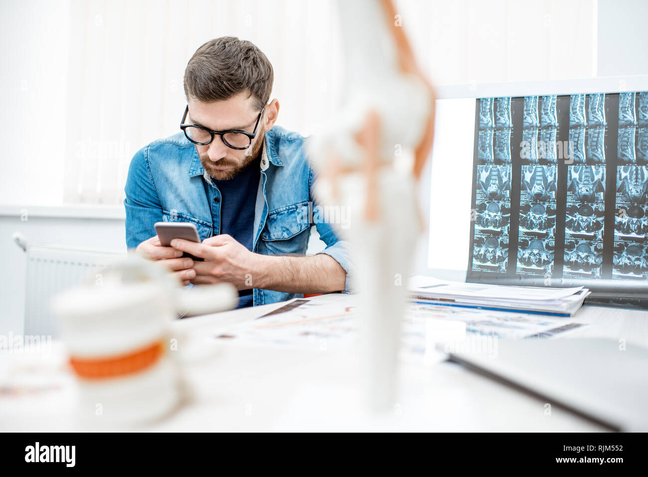 Mann mit Smartphone nach unten gebeugt sitzen in die Skoliose im Büro des Therapeuten in der Klinik Stockfoto