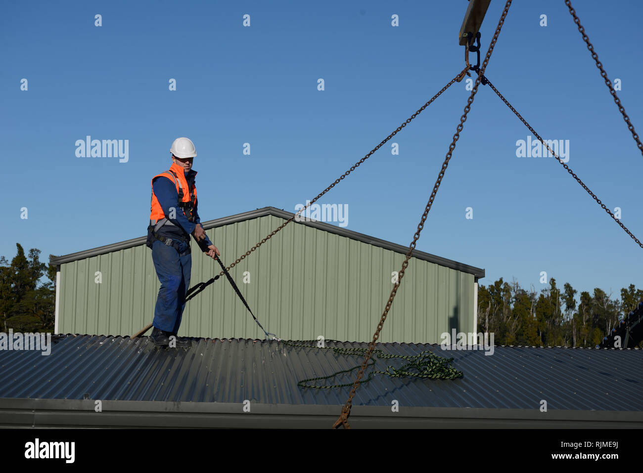 Ein Bauherr trägt ein sicherheitsgeschirr hilft die Schlinge für ein Kran einen tragbaren Gebäude zu platzieren Stockfoto