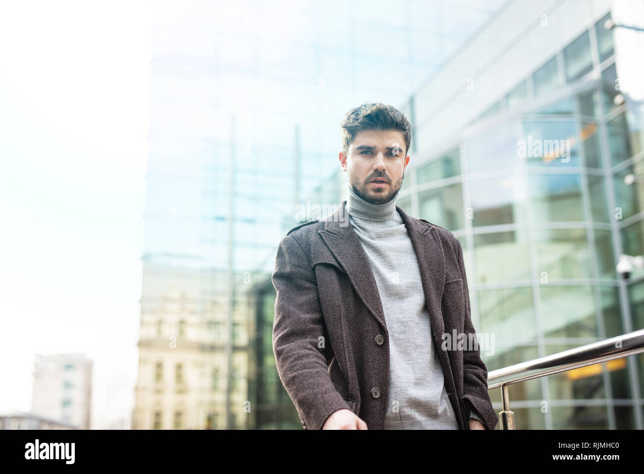 Junge Unternehmer auf der Suche zuversichtlich, mit Bürogebäude hinter ihm, auf der Suche entspannt. Erfolgreiche stilvollen Mann Stockfoto