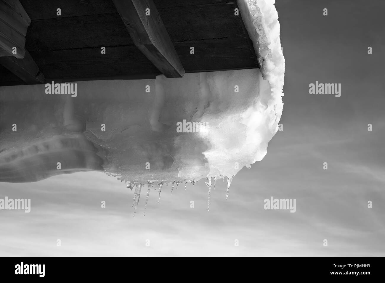 Schwarze und weiße Holzdach mit nach unten hängen Schnee Gesims und Icicle bei Sun winter Tag Stockfoto