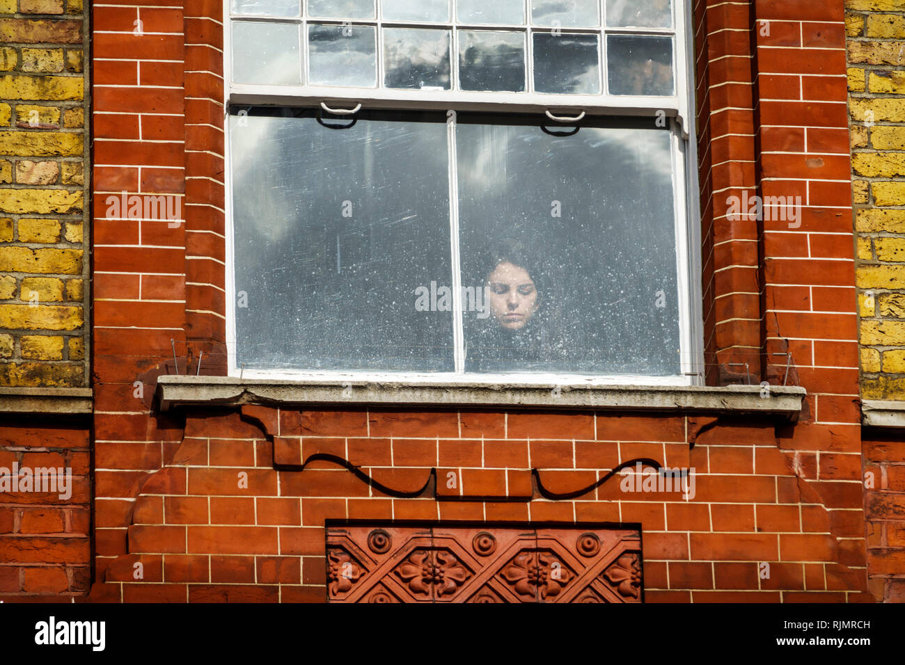Vereinigtes Königreich Großbritannien England London Kensington Backsteinfenster Frau, die durch das Fenster schaute, mit geschlossenen Augen, um Besucher zu besichtigen Stockfoto