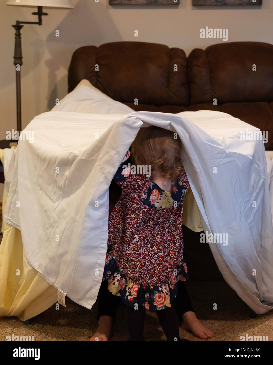 Zwei kaukasische Mädchen Kinder spielen mit behelfsmäßigen Hütte aus ein Blatt über Möbel drinnen drapiert. Stockfoto