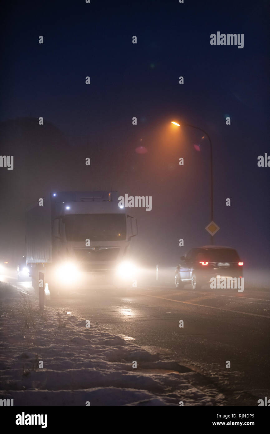 Leuchtendes Auto- und LKW-Scheinwerfern in der Nacht im Nebel im Winter Straße. Stockfoto
