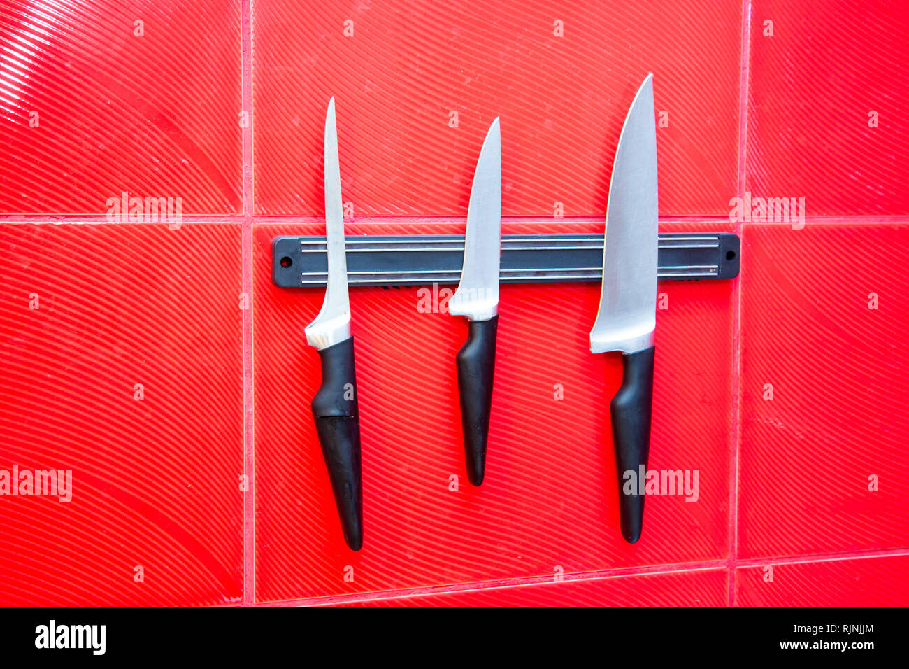 Qualitativ hochwertige Küche kochen Messer Werkzeuge auf einer Magnettafel hängen an der Roten Wand Stockfoto