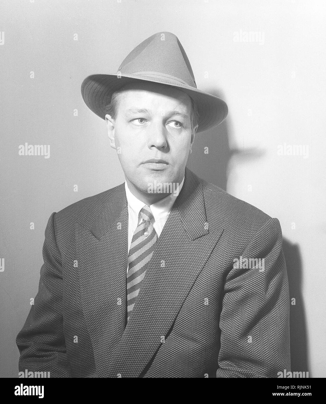 Hut Mode in den 50er Jahren. Ein Mann in Anzug und Krawatte trägt ein  Fedora Art hat. Einen weichen Rand und in der Regel gefaltet längs und in  der Nähe der vorderen