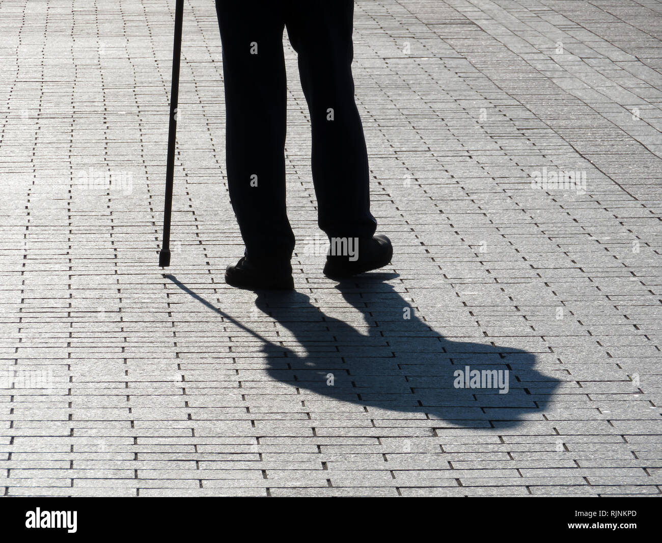 Silhouette der Mann mit einem Stock, lange Schatten auf Pflaster. Konzept der hinkt oder blind Person, Behinderung, Alter, Erkrankungen der Wirbelsäule Stockfoto