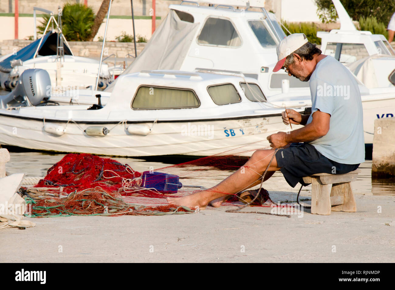 Insel Prvic, Kroatien - 23. August 2018: Fischer Instandsetzung seiner Fischernetz auf Pier mit Booten im Hintergrund Stockfoto