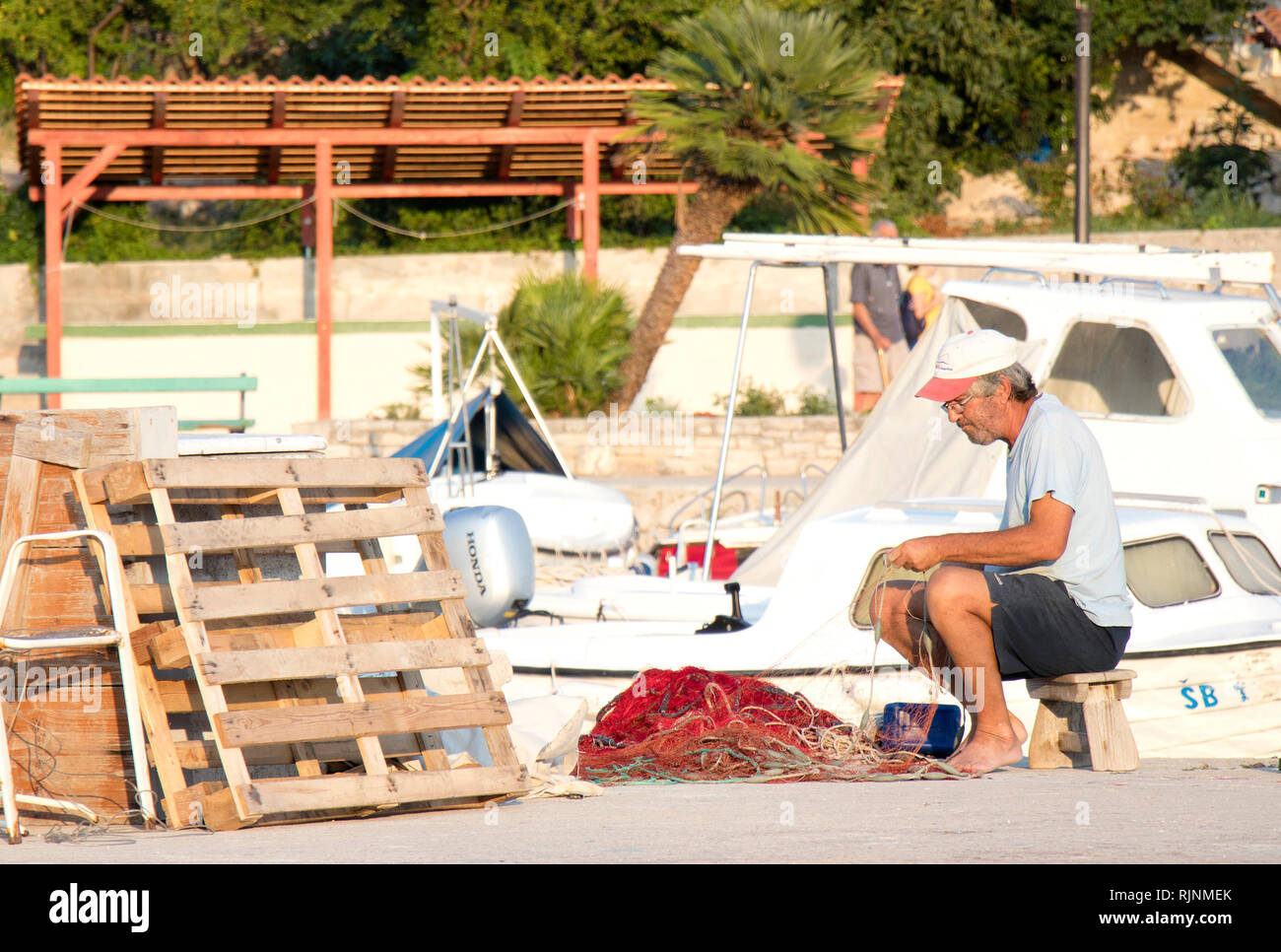 Insel Prvic, Kroatien - 23. August 2018: Fischer Instandsetzung seiner Fischernetz auf Pier mit Booten im Hintergrund Stockfoto