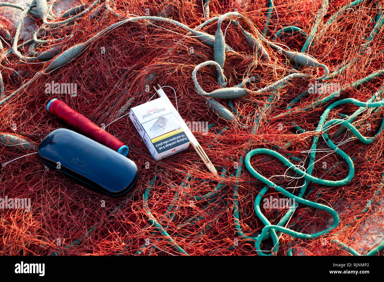 Insel Prvic, Kroatien - 23. August 2018: Fischer" Zubehör, rot Fischernetz mit Einwebung Nadel, Brillen, Zigaretten auf dem Pier in Sun Stockfoto