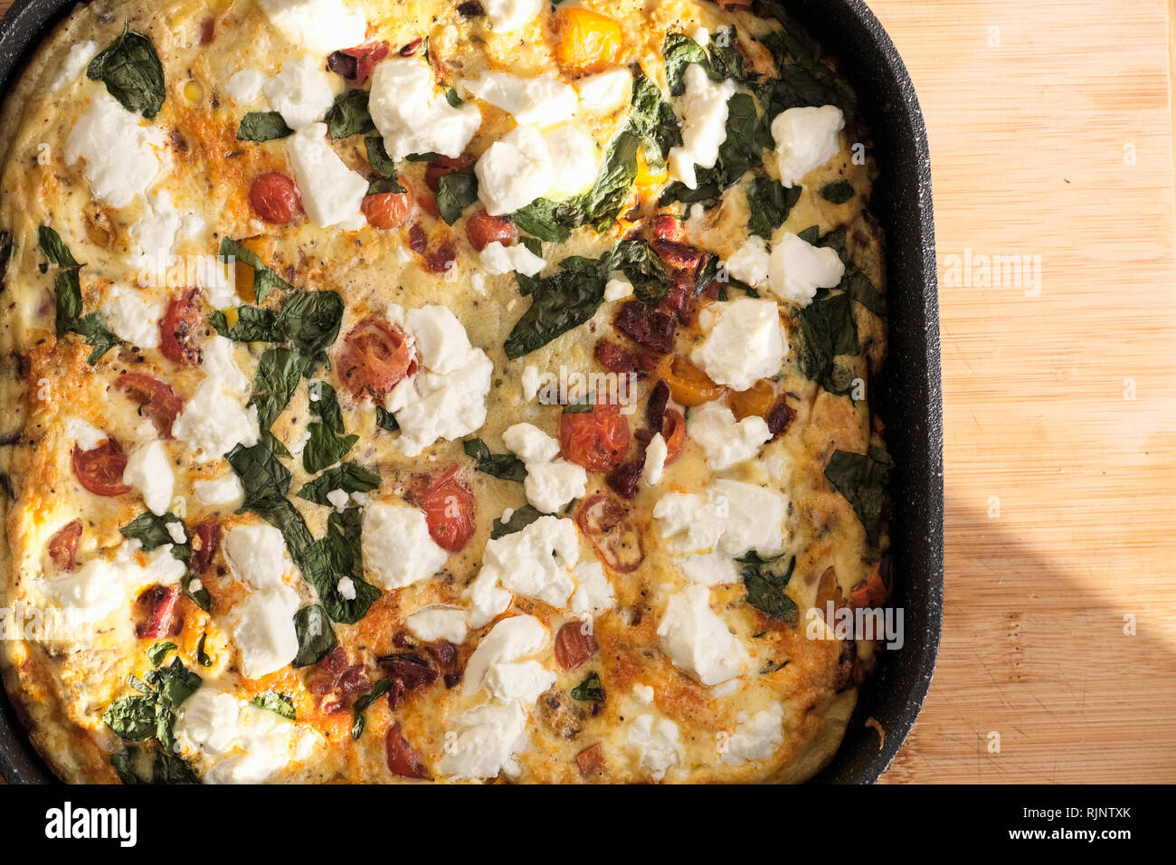 Ein frisch zubereitetes frittata mit geschlagenen Eier, Ziegen Käse Tomaten, frischem Basilikum. Es ist immer noch heiß in der Pfanne zu kochen Stockfoto